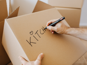 A man is writing kitchen on a moving box